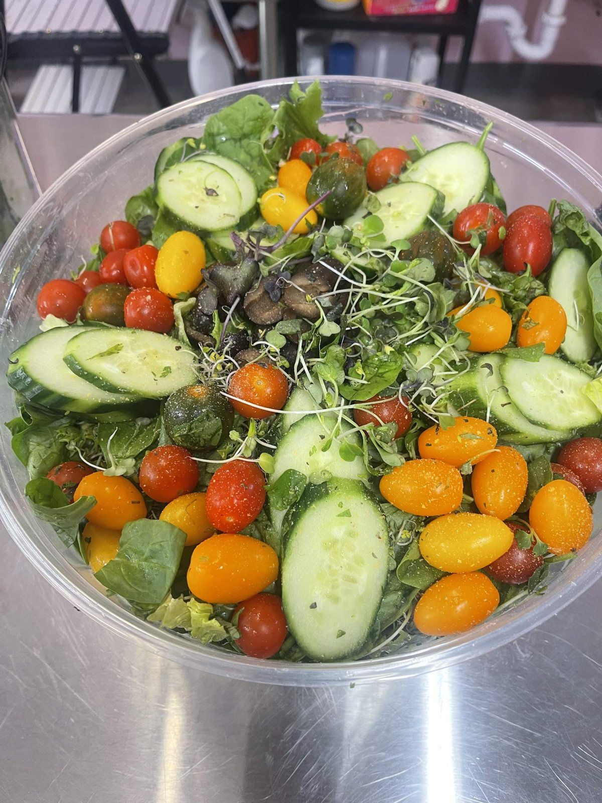 A large bowl of garden salad with cucumber, colourful cherry tomatoes and microgreens